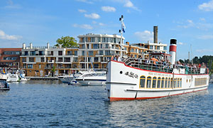 Dampfer der Weißen Flotte bring Fahrgäste in den Stadthafen von Waren, im Hintergrund Ferienappartments als Kontrastprogramm zur ansehnlichen Altstadt